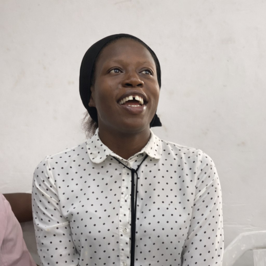 Person smiling indoors, wearing a patterned blouse and head covering.