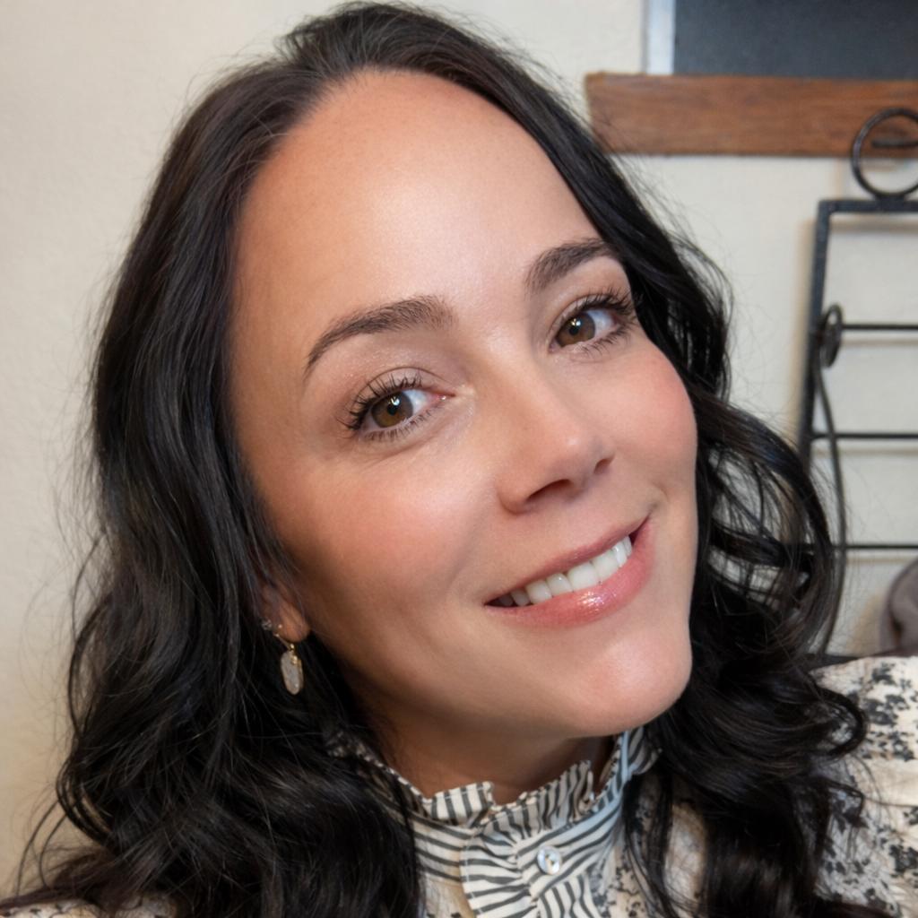 Smiling woman with dark hair in a patterned blouse, photographed indoors.