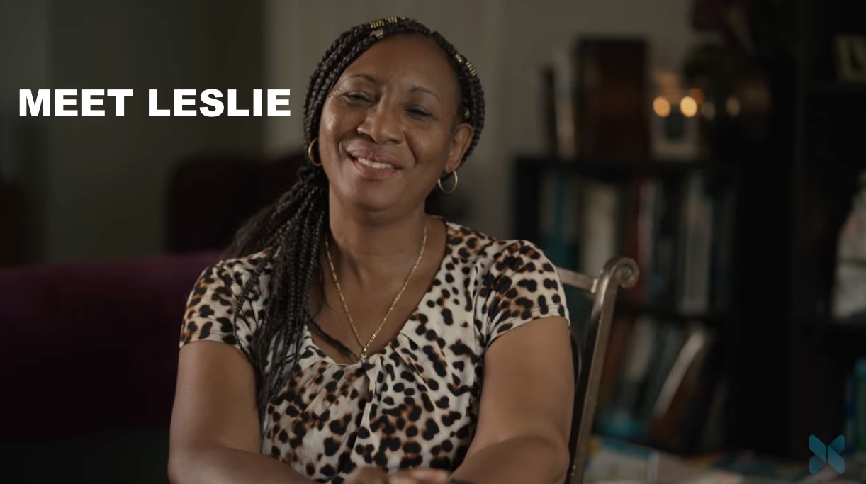 A smiling woman sits in a chair indoors with the words “Meet Leslie” displayed on the screen.