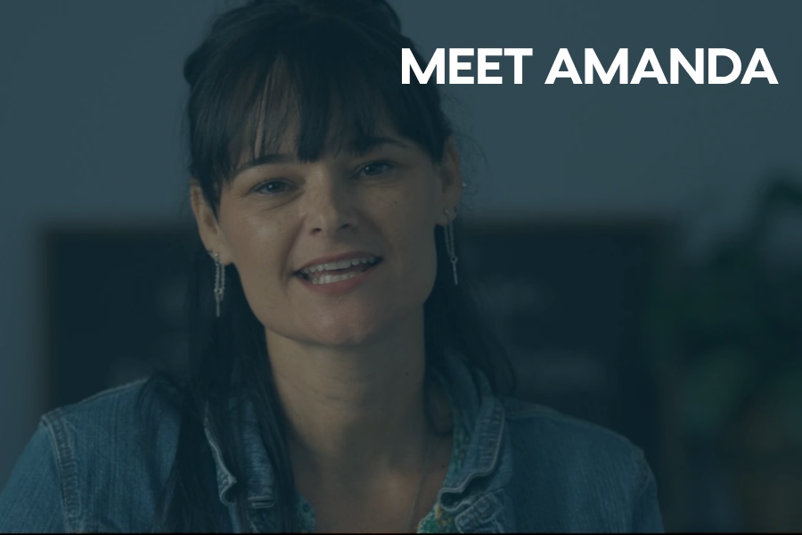 Woman smiling in a softly lit indoor setting, wearing a denim jacket, with the text “MEET AMANDA” displayed on the right side.